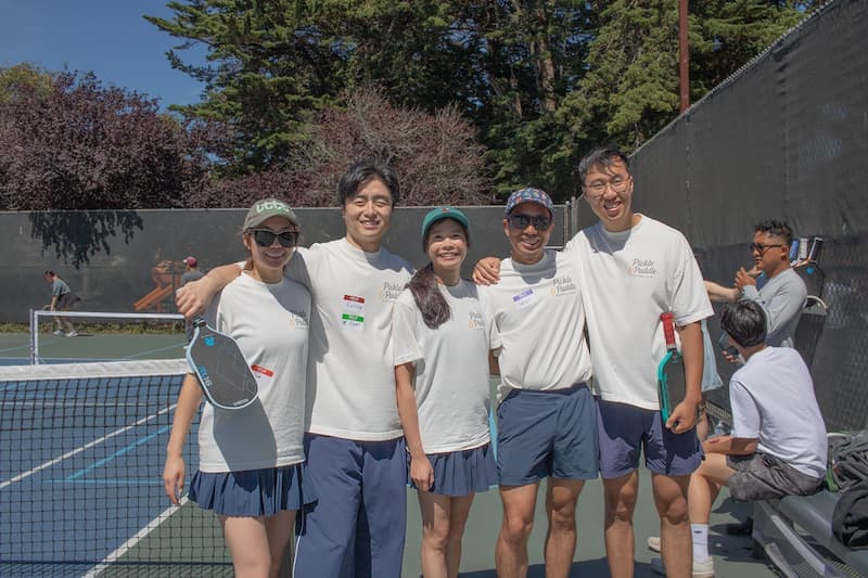 Five club members posing together on court with paddles