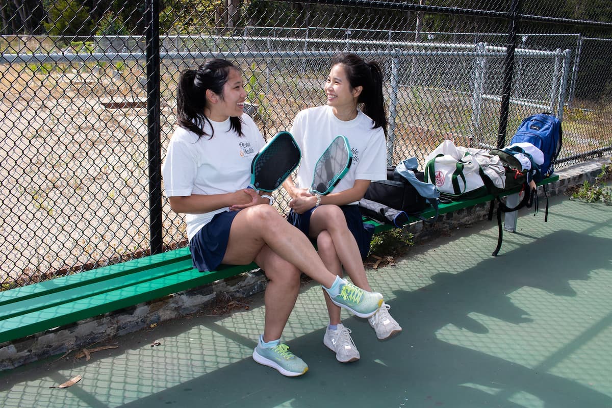Two members laughing on a courtside bench between games